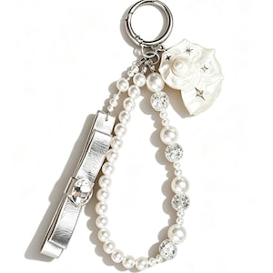 May include: A keychain featuring a silver metal ring, a white shell charm with star accents, a strand of white faux pearls, a strand of alternating faux pearls and clear faceted beads, and a silver metallic bow with a central clear crystal.