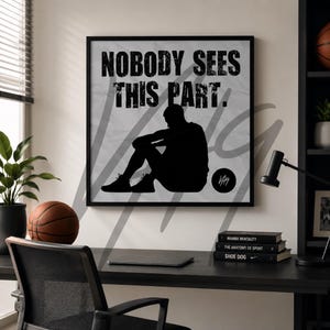 Może przedstawiać: Czarna oprawiona grafika ścienna z napisem „NOBODY SEES THIS PART”. Grafika przedstawia czarną sylwetkę osoby siedzącej ze spuszczoną głową. Piłka do koszykówki leży na biurku przed grafiką.
