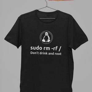 Może przedstawiać: Czarny t-shirt z krótkim rękawem z białą grafiką przedstawiającą logo pingwina Linux Tux oraz napis "sudo rm -rf /" i "Don't drink and root" wydrukowany czystą czcionką bezszeryfową na środku klatki piersiowej.