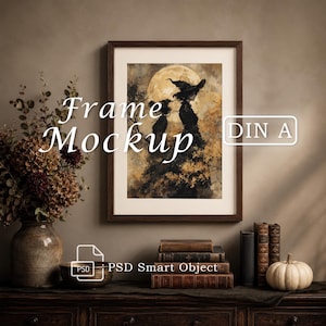 May include: A dark brown wooden frame containing a print of a witch silhouette against a large full moon. The text "Frame Mockup" and "DIN A" are overlaid. Below the frame are stacked antique books, a small pumpkin, and a ceramic vase.