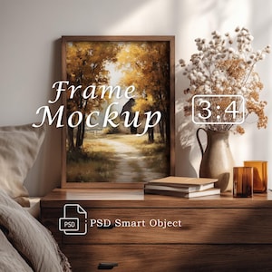 May include: A vertical wooden picture frame containing an art print of a path through autumn trees, with the text Frame Mockup and 3:4 displayed. Beside the frame is a ceramic vase with dried flowers, two stacked books, and a glass tumbler.