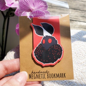 May include: A handmade magnetic bookmark featuring a black and red moth illustration. The bookmark is on a brown card with the text "handmade MEGNETIC BOOKMARK".