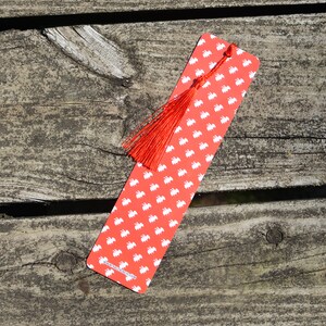 May include: Red bookmark with a white pattern of small animals and a red tassel. The bookmark has the text "www.etsy.com/shop/fancy" printed on the bottom.
