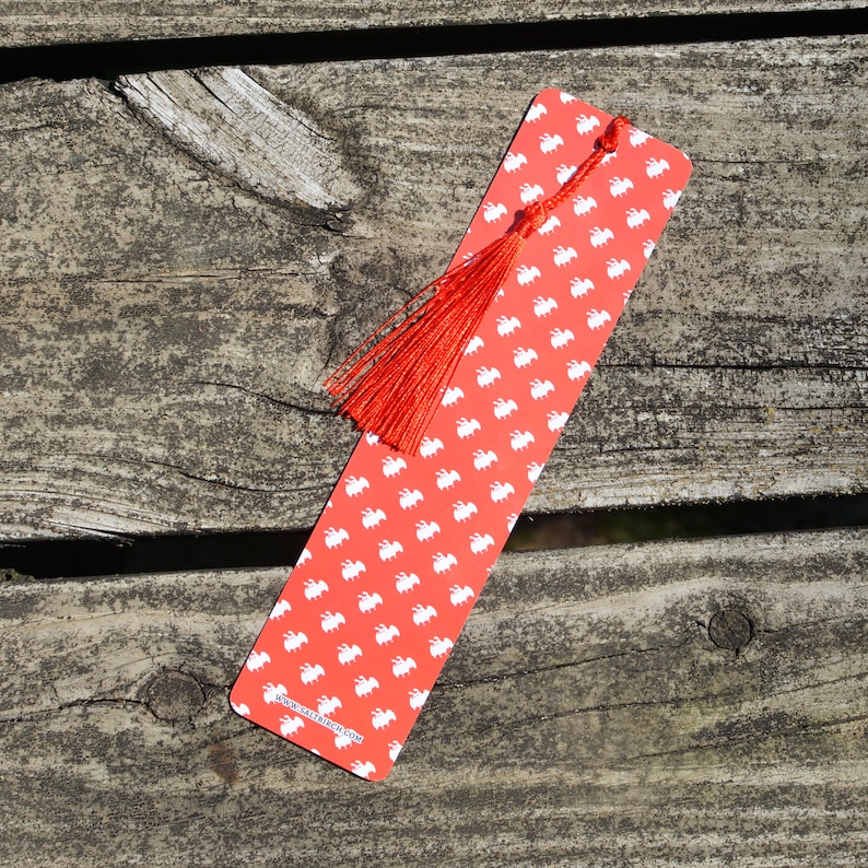 May include: Red bookmark with a white pattern of small animals and a red tassel. The bookmark has the text "www.etsy.com/shop/fancy" printed on the bottom.
