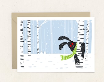 May include: Greeting card featuring a whimsical illustration of a black creature with red eyes wearing a green scarf, peeking from behind a birch tree in a snowy forest. The background shows a light blue sky and falling snow.