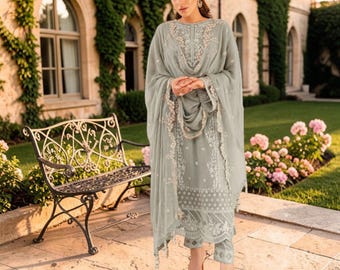 Puede incluir: Un conjunto de tres piezas en color verde salvia que incluye una túnica de manga larga con intrincados bordados florales blancos, pantalones rectos a juego y una dupatta transparente coordinada drapeada sobre los hombros con bordes de encaje festoneado.