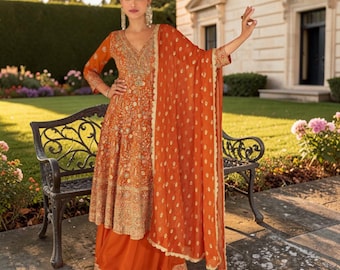 Può includere: Un vivace completo arancione a tre pezzi composto da una tunica al ginocchio con intricati ricami dorati, una gonna arancione in tinta unita con un ampio orlo ricamato e un dupatta arancione trasparente decorato con piccoli motivi dorati.