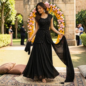 May include: A black floor-length dress featuring a fitted bodice with intricate sequin embellishments and a front slit. The garment includes a long, flowing skirt and a matching sheer black dupatta held to the side, creating a layered silhouette.
