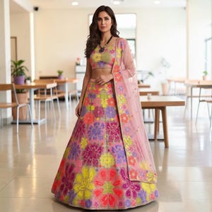 May include: A colourful lehenga featuring a floral pattern in pink, yellow, purple, and orange. The outfit includes a matching crop top and a sheer, light pink dupatta. This traditional Indian garment is suitable for special events and celebrations.