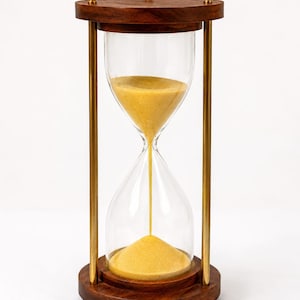 May include: An hourglass with a wooden frame and base, featuring clear glass chambers and brass-colored metal supports. The hourglass contains yellow sand, currently flowing from the top chamber to the bottom. The wooden elements have a rich, dark brown finish.
