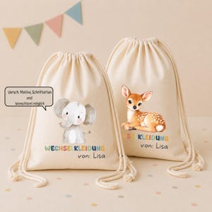 Può includere: Due sacche in tessuto color bianco sporco con chiusura a coulisse. Una sacca presenta l'illustrazione di un elefante grigio con il testo "WECHSELKLEIDUNG von: Lisa". L'altra sacca mostra l'illustrazione di un cerbiatto marrone con il testo "WECHSELKLEIDUNG von: Lisa".