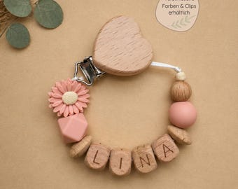 Catena per ciuccio in legno personalizzabile con nome e fiore, disponibile in vari colori e con diverse clip per bambini e bambine, con sacchetto regalo incluso.