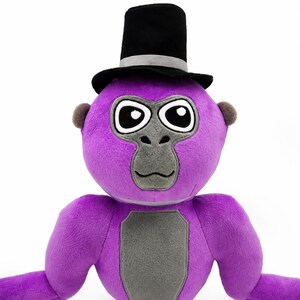 May include: A plush gorilla toy featuring bright purple fur, a gray face, and a gray chest patch. The gorilla has large black and white eyes and is wearing a black top hat with a silver band. The toy has small brown ears and long arms.