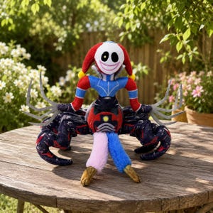 May include: A plush toy featuring a white jester-like head with a wide smile and one yellow eye, wearing a red and blue outfit. The figure has multiple dark patterned spider-like legs, long grey clawed hands, and two lower legs in light pink and blue.
