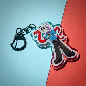 Puede incluir: Un llavero acrílico transparente con un personaje de dibujos animados con camisa azul, pantalón negro y bufanda roja. El llavero tiene un cierre negro y una anilla partida. El personaje tiene una cabeza blanca, una estrella y un ojo morado.