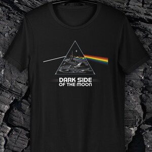 Könnte beinhalten: Schwarzes T-Shirt mit einem grafischen Design. Das Design umfasst ein weißes Dreieck, eine Mondlandschaft, einen Regenbogen und den Text "DARK SIDE OF THE MOON". Das Design ist mittig auf der Vorderseite.
