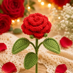 Puede incluir: Una rosa roja hecha a mano con hojas y tallo verdes. La rosa está en plena floración, mostrando costuras detalladas. Las hojas son de un verde vibrante y el tallo es de un verde más oscuro. Pétalos de rosa rojos dispersos.