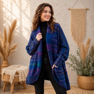 May include: A blue, purple, and teal patterned cardigan with pockets. The open-front sweater has a shawl collar and is worn over a black turtleneck and black pants. The cardigan is a cozy, long-sleeved garment.