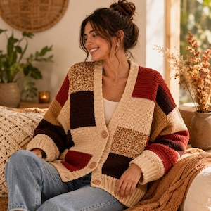 May include: A patchwork crochet cardigan in beige, brown, and red tones. The open-front sweater features large square blocks of color and wooden buttons. The cozy, handmade garment is perfect for fall and winter.