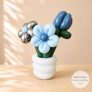 May include: A balloon sculpture featuring three flowers in a white balloon vase. One flower is metallic silver, one is light blue with a dark blue centre, and one is a dark blue tulip shape. The stems are dark green balloons.