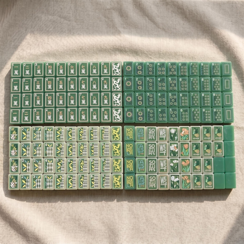 May include: A set of green Mahjong tiles arranged in four rectangular blocks. The tiles feature various designs including Chinese characters, numeric dots, bamboo patterns, directional text like North, South, East, West, and floral illustrations.
