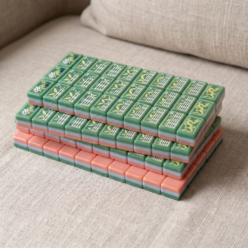 May include: A set of rectangular mahjong tiles stacked in four rows. The top tiles feature green surfaces with white bamboo, numerical, and dragon engravings. Each tile has a layered design with a green middle section and a pink base.