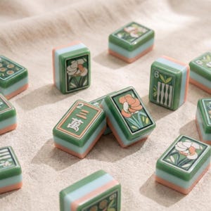 May include: A collection of rectangular mahjong tiles featuring green, light blue, and peach-colored layers. The tiles display various illustrations including floral patterns, bamboo stalks, and the Chinese characters for the number two and ten thousand.