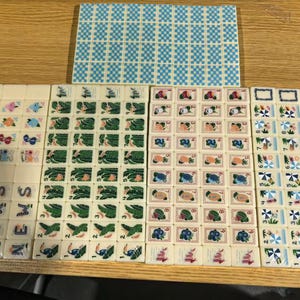 May include: A collection of rectangular mahjong tiles arranged in rows and columns. The tiles feature various colorful illustrations including tropical plants, fruits, beach umbrellas, and the word NEWS. One large rectangular tile has a blue checkered pattern.