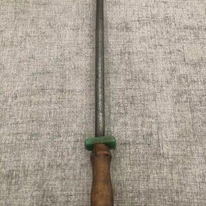 May include: A knife sharpening steel with a wooden handle and a green bolster. The steel is long and cylindrical, designed for honing the edge of knives. The handle has a loop for hanging.