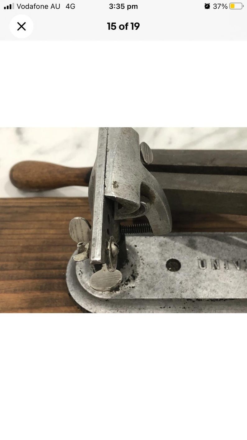 May include: Close-up of a vintage metal tool with a wooden handle. The tool has a silver finish and features adjustable parts, including a screw and a circular base. The word "UNIV" is visible on the base.