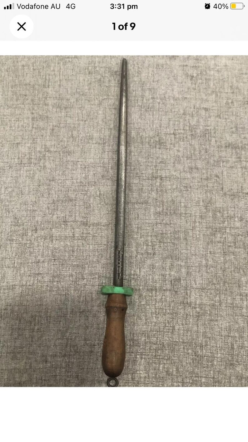 May include: A steel knife sharpening rod with a wooden handle and a green plastic guard. The rod is long and slender, designed for honing the edge of knives. The handle is a dark brown color.
