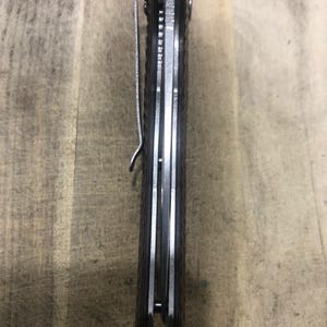 May include: A closed pocket knife with a brown handle and a silver pocket clip. The knife has a textured handle and a silver blade. The knife is shown from a side view.
