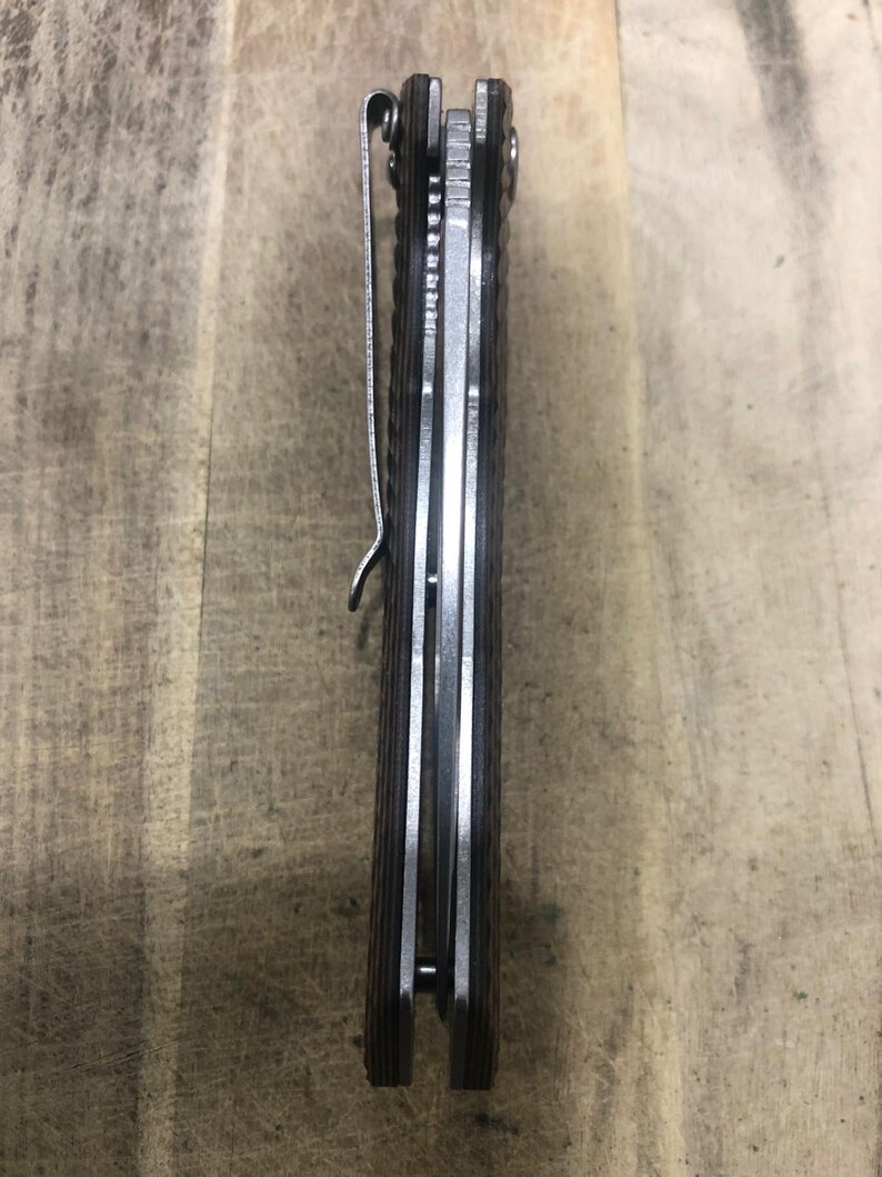 May include: A closed pocket knife with a brown handle and a silver pocket clip. The knife has a textured handle and a silver blade. The knife is shown from a side view.