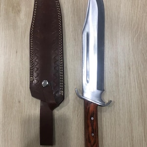 以下が含まれることがあります： 光沢のある鋼の刃と木製の柄が付いた大型の狩猟用ナイフ。濃い茶色の革製の鞘が付属しています。ナイフには銀色のガードが付いています。