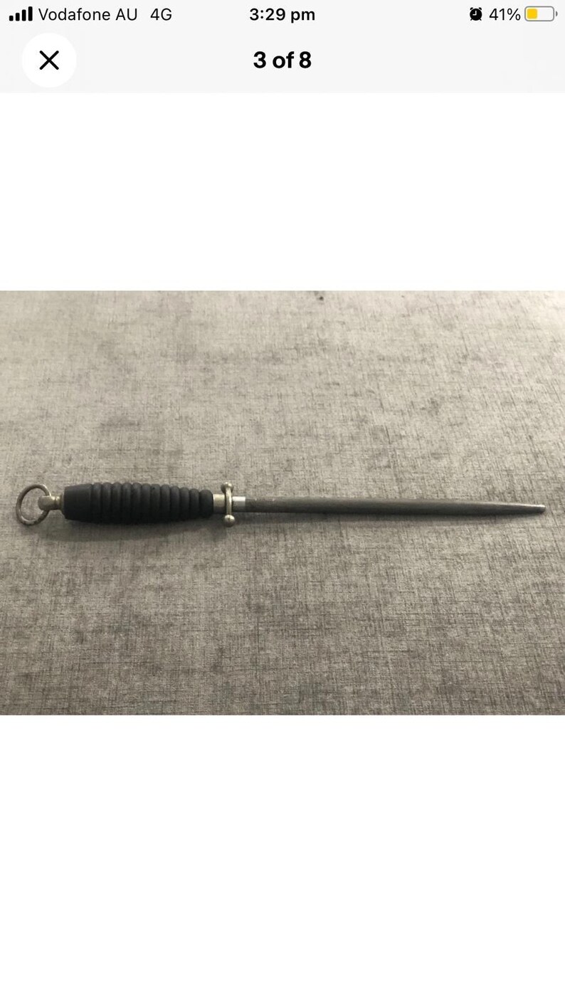 May include: A black and silver knife sharpening steel. The handle is black with a ridged design, and the steel is a slender, tapered rod. A small silver ring is at the end of the handle.