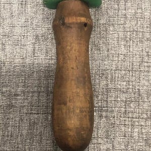 May include: A vintage knife sharpener with a wooden handle and a green rectangular stone. The handle is a dark brown color with a metal ring at the bottom. The sharpener is designed for sharpening knives.