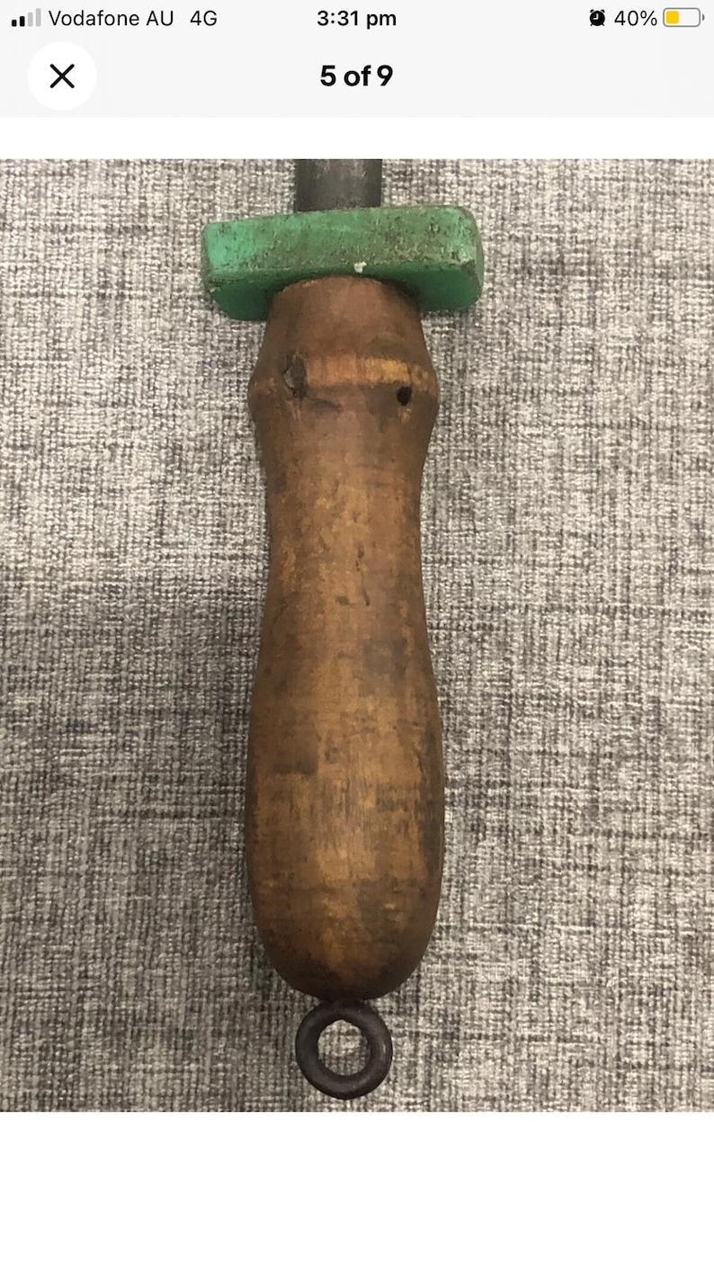 May include: A vintage knife sharpener with a wooden handle and a green rectangular stone. The handle is a dark brown color with a metal ring at the bottom. The sharpener is designed for sharpening knives.
