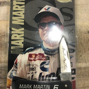 Könnte beinhalten: Ein Sammler-Case-Messer mit Mark Martin, verpackt in einer transparenten Kunststoffhülle. Das Messer hat einen schwarzen Griff mit dem Aufdruck "MARK MARTIN 6". Die Verpackung enthält ein Foto von Mark Martin in einem Rennanzug.
