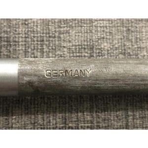 May include: Close-up of a metal object with the word "GERMANY" stamped on it. The object has a silver end and a textured, gray body. The background is a textured, gray surface.