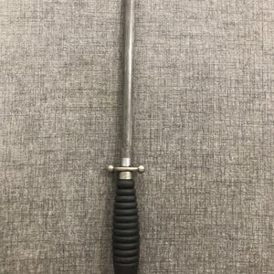 May include: A silver steel knife sharpener with a black, ridged handle and a small metal loop at the base. The sharpener has a long, tapered steel rod and a decorative metal guard.