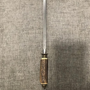 May include: A knife sharpening steel with a long, silver blade and a handle made of brown and tan antler material. The handle has a brass-colored bolster and a small metal loop at the end.