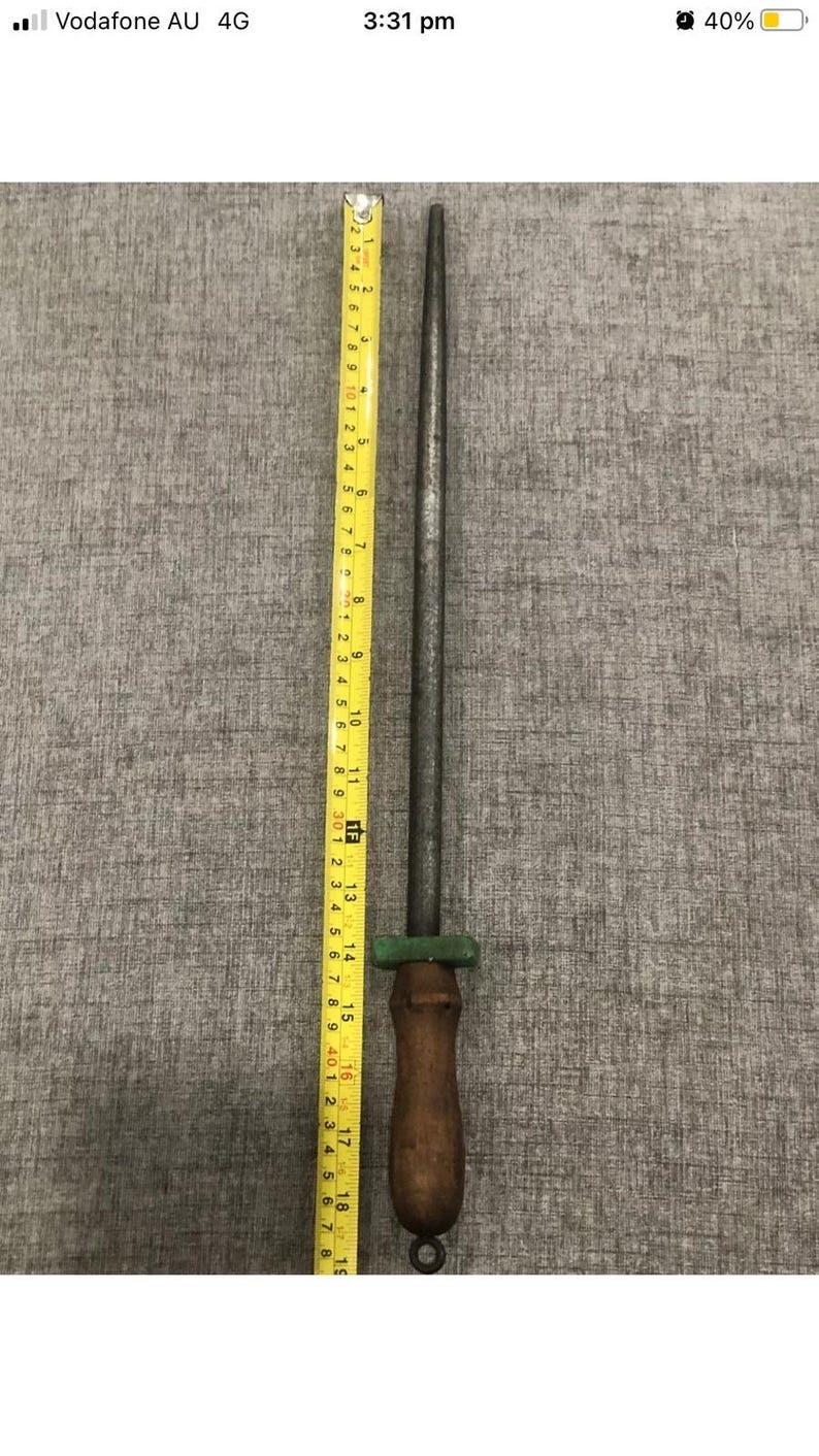 May include: A steel knife sharpening rod with a wooden handle. The rod is approximately 15 inches long, with a green guard and a loop at the end of the handle. A yellow measuring tape is next to the rod.