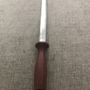 Pode incluir: Uma afiadora de facas com uma haste de a&ccedil;o branca e um cabo castanho escuro. O cabo tem um anel para pendurar. O a&ccedil;o est&aacute; marcado "MADE IN W-GERMANY".