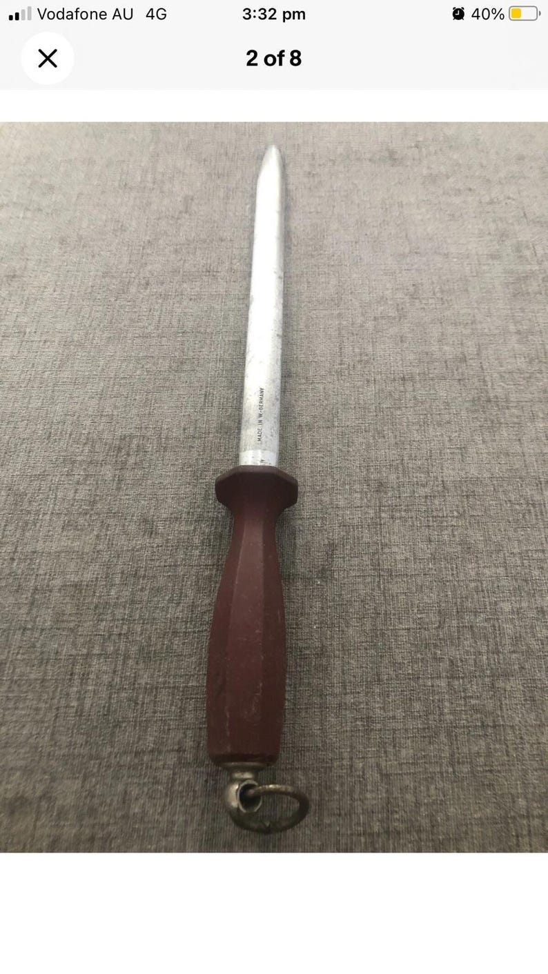 Pode incluir: Uma afiadora de facas com uma haste de a&ccedil;o branca e um cabo castanho escuro. O cabo tem um anel para pendurar. O a&ccedil;o est&aacute; marcado "MADE IN W-GERMANY".