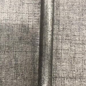 May include: A close-up of a metal pole with a textured, slightly rough surface. The pole is a dark gray color and appears to be made of steel or a similar material. The background is a gray, textured fabric.