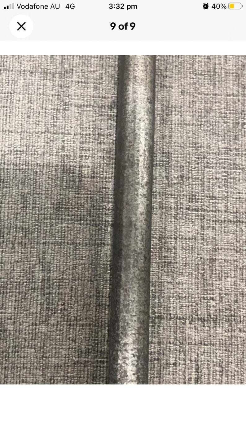 May include: A close-up of a metal pole with a textured, slightly rough surface. The pole is a dark gray color and appears to be made of steel or a similar material. The background is a gray, textured fabric.