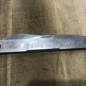 May include: A vintage silver pocket knife with two blades. The knife has a rectangular body with a small brass rivet on one end and a black rivet on the other. The word "Japan" is stamped on the side.