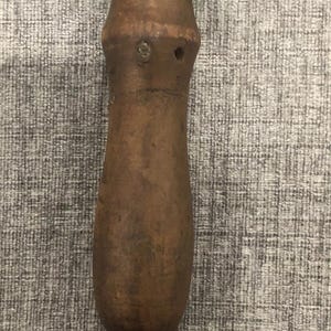 May include: A wooden tool with a brown handle and a green top. The handle has a ring at the bottom. The tool appears to be vintage or antique.