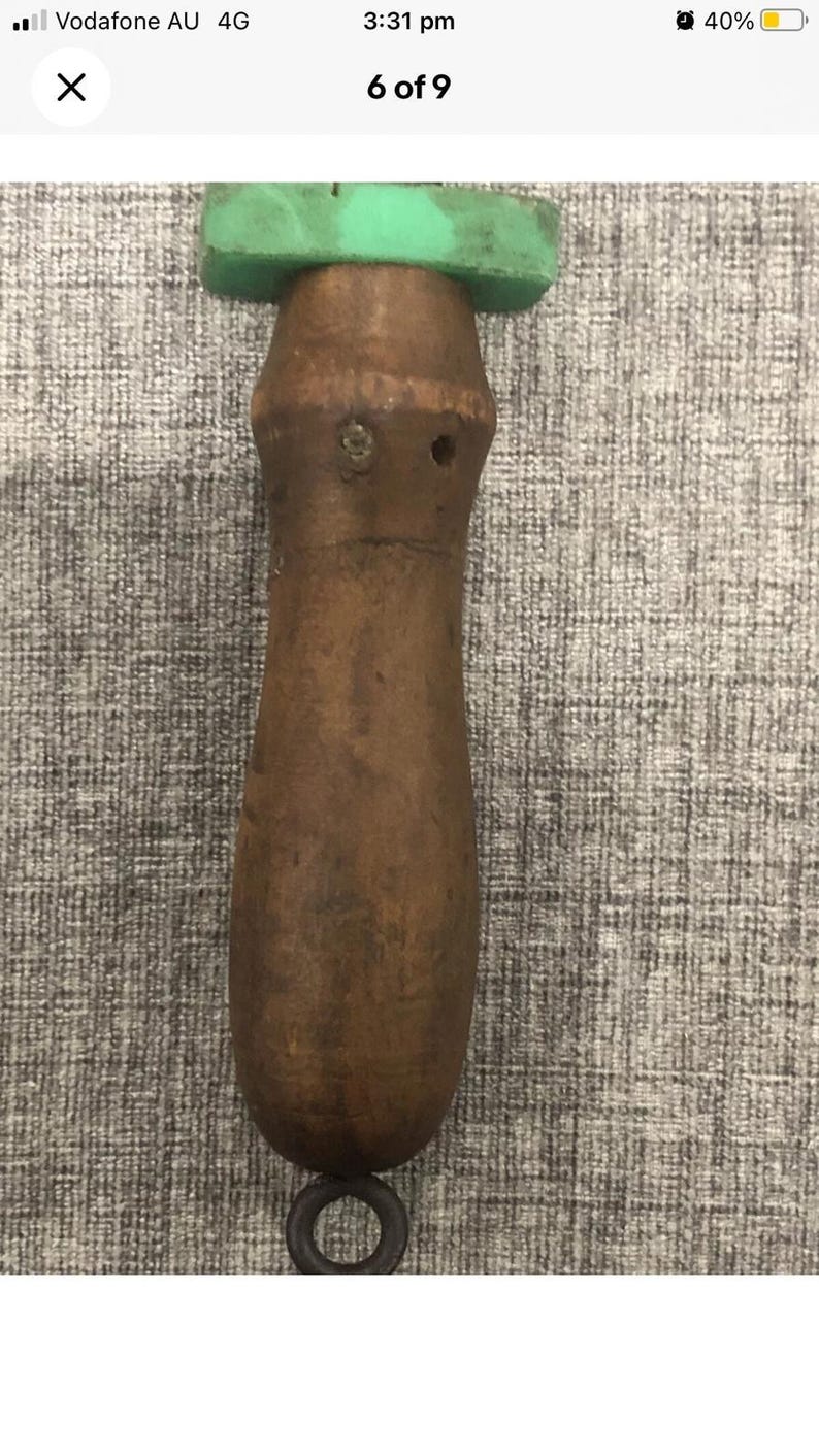 May include: A wooden tool with a brown handle and a green top. The handle has a ring at the bottom. The tool appears to be vintage or antique.