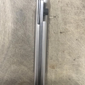 Pode incluir: Uma faca dobr&aacute;vel prateada fechada com um parafuso preto. A faca tem uma forma retangular e um acabamento met&aacute;lico liso. A l&acirc;mina n&atilde;o &eacute; vis&iacute;vel nesta imagem.